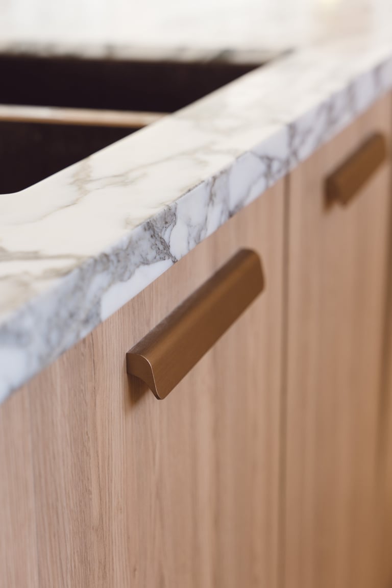 Close-up of marble countertop with bronze handle on light wood cabinetry in a modern kitchen