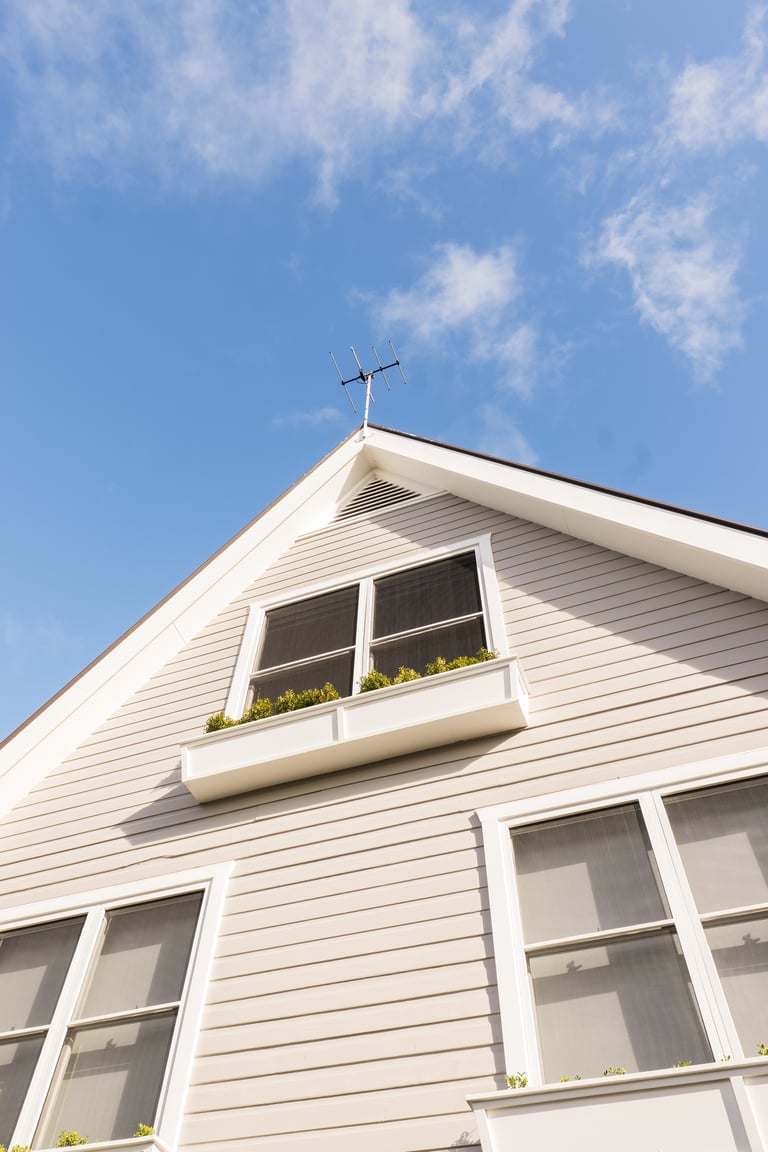 White house with gabled roof and cross antenna against blue sky with white clouds