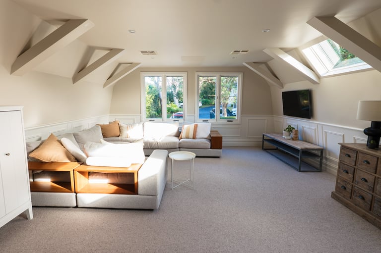 Modern attic living room with vaulted ceilings, skylights, comfortable seating, and large windows overlooking greenery