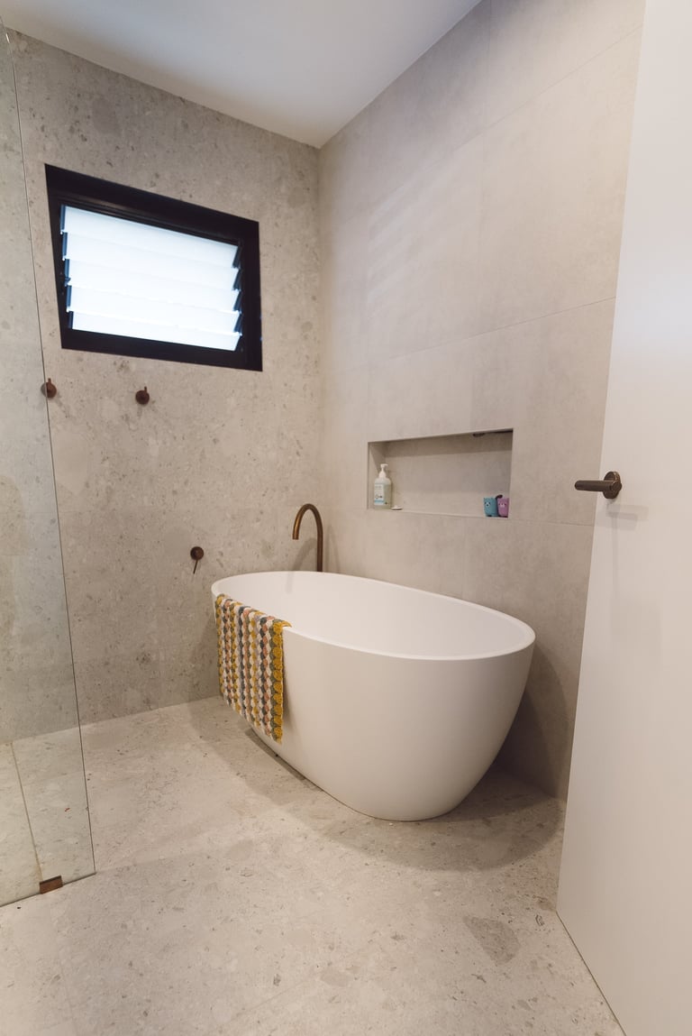 Modern bathroom with freestanding white oval bathtub, concrete walls, rectangular window, and walk-in shower with glass door.