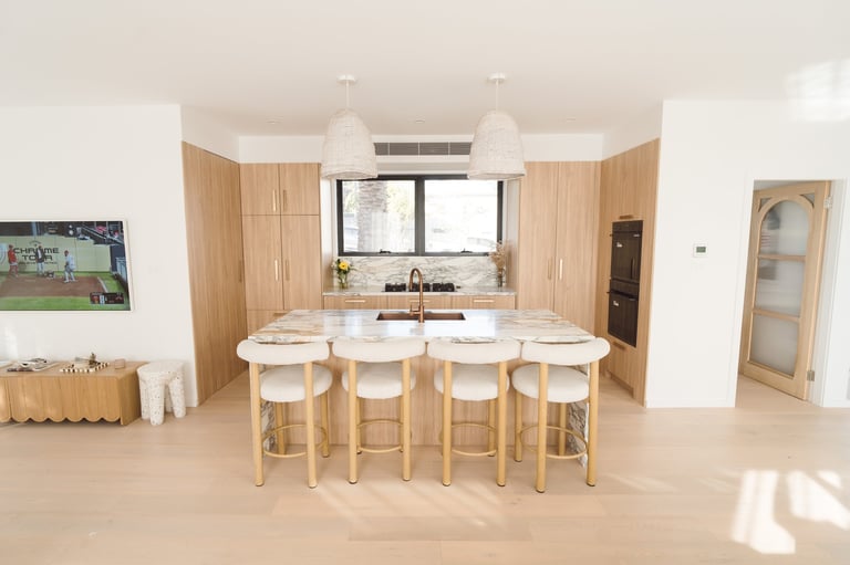 Modern kitchen with light wood cabinetry, marble island with four bar stools, and pendant lighting overhead