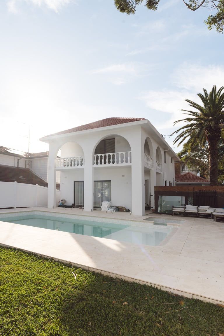 Modern white villa with arched colonnade, pool, and palm tree in sunny residential setting