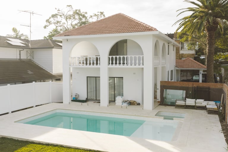 Modern white two-story house with curved balcony and turret, featuring a blue swimming pool in the front yard