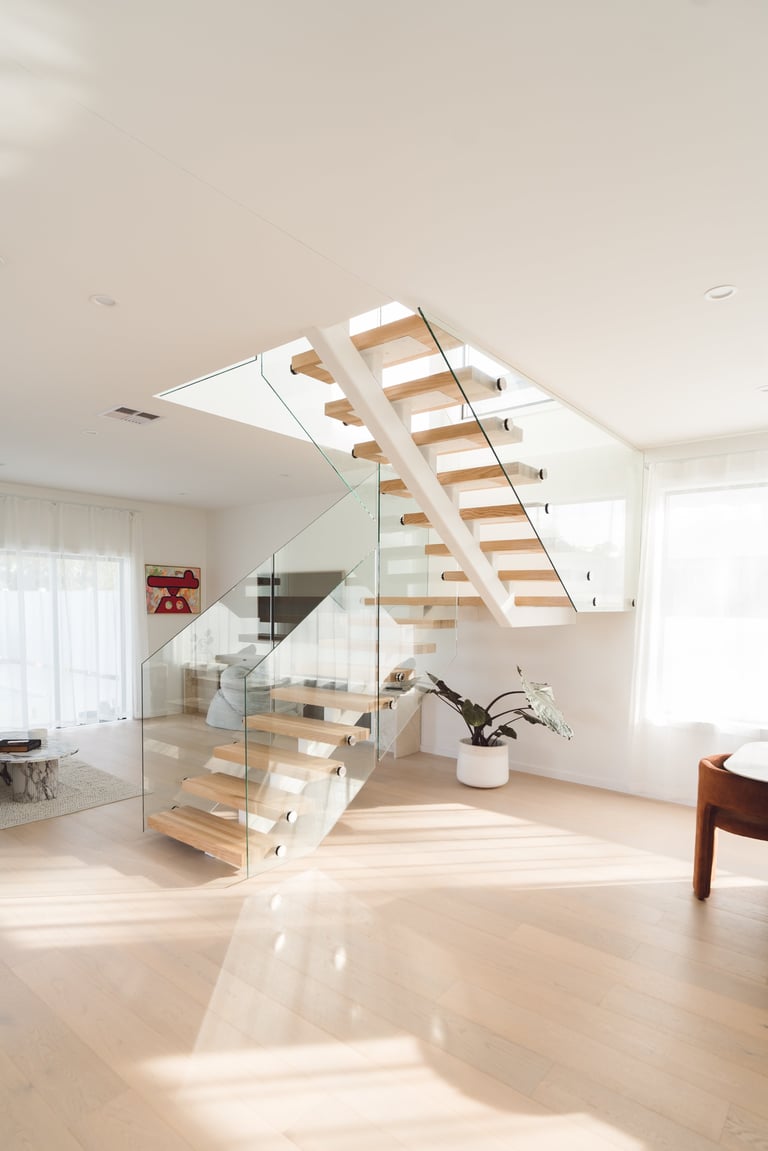 Modern staircase with wood steps and glass railings in a bright, minimalist interior with skylight