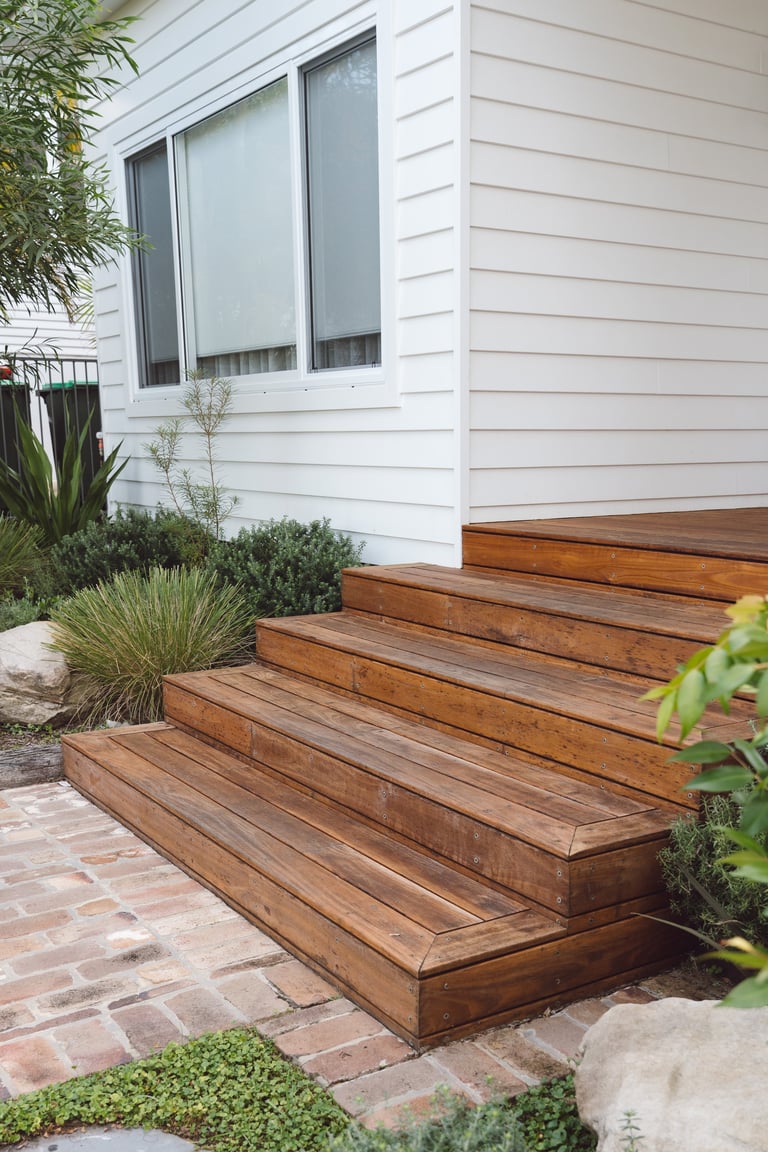 Wooden deck steps leading to a modern white house with landscaping and potted plants on the sides