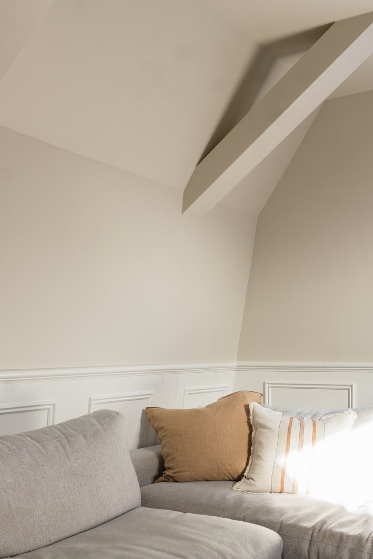 Modern minimalist bedroom corner with gray upholstered furniture, decorative pillows, and angled ceiling with white trim detailing