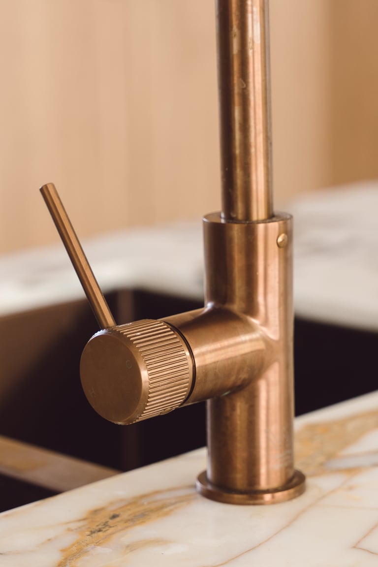 Bronze kitchen faucet with single lever handle mounted on a light wood countertop above a black sink