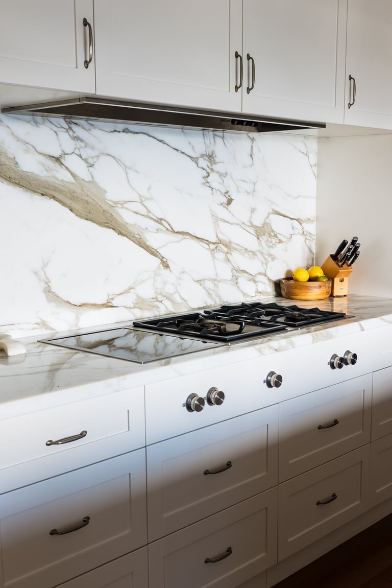 Modern kitchen with white cabinetry, marble backsplash, gas cooktop, and wooden utensil holder with lemons on countertop