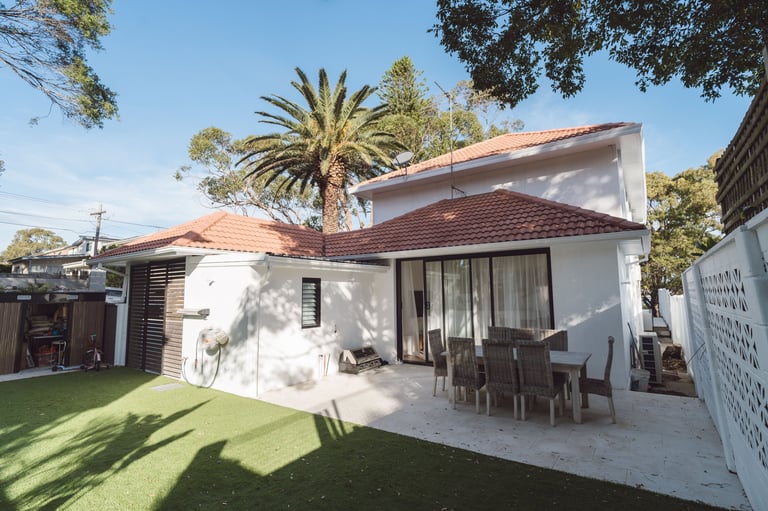 Modern white house with terracotta roof, outdoor patio area, palm tree, and manicured lawn in bright daylight