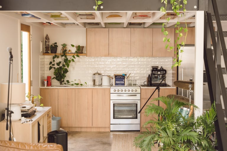 Modern light wood kitchen with white appliances, brick backsplash, and hanging green plants throughout