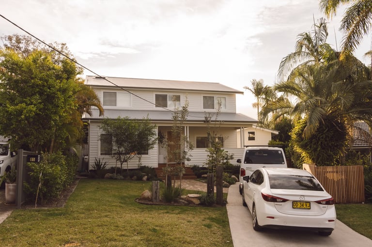 White two-story residential house with palm trees and vehicles parked on driveway in suburban setting