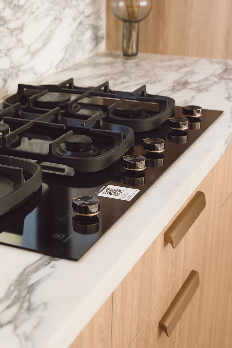 Black gas cooktop with stainless steel knobs installed on a marble countertop in a modern kitchen