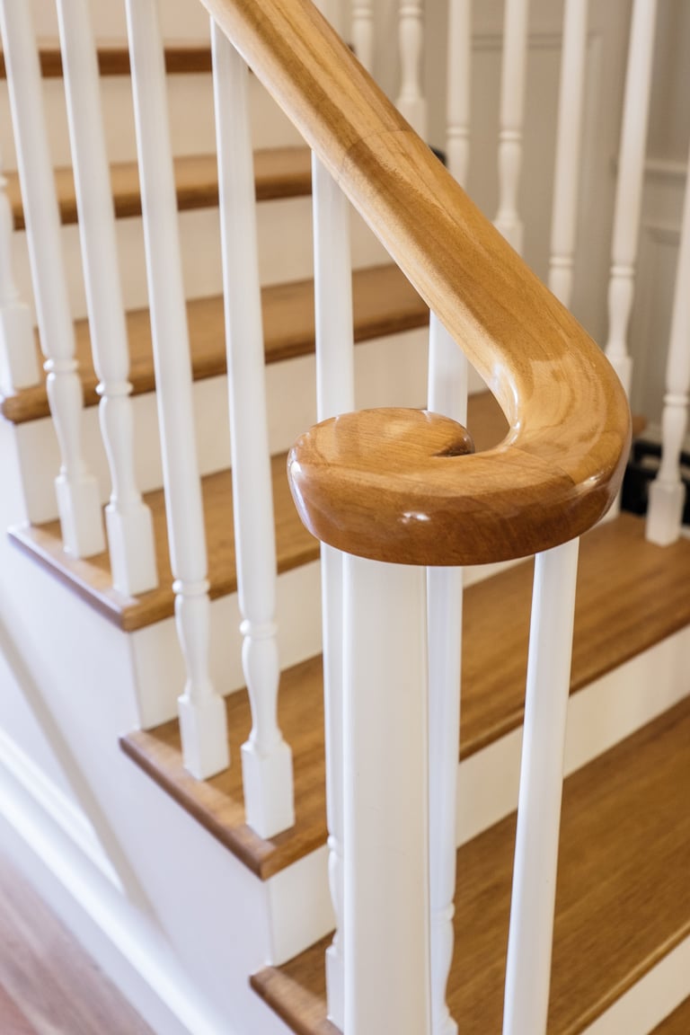 Close-up of wooden stair railing with curved handrail and white balusters
