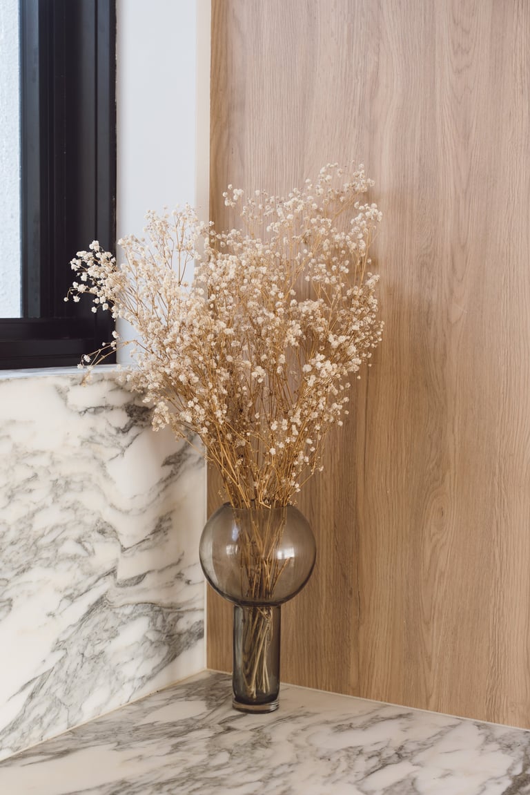 Dried babys breath flowers in a dark glass vase on a marble surface against a wood-paneled wall