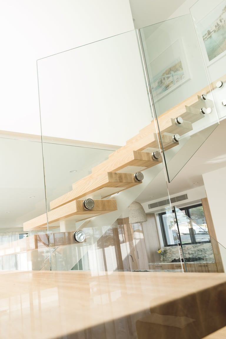 Modern staircase with light wood steps, glass railings, and metal fixtures in a bright, minimalist interior space