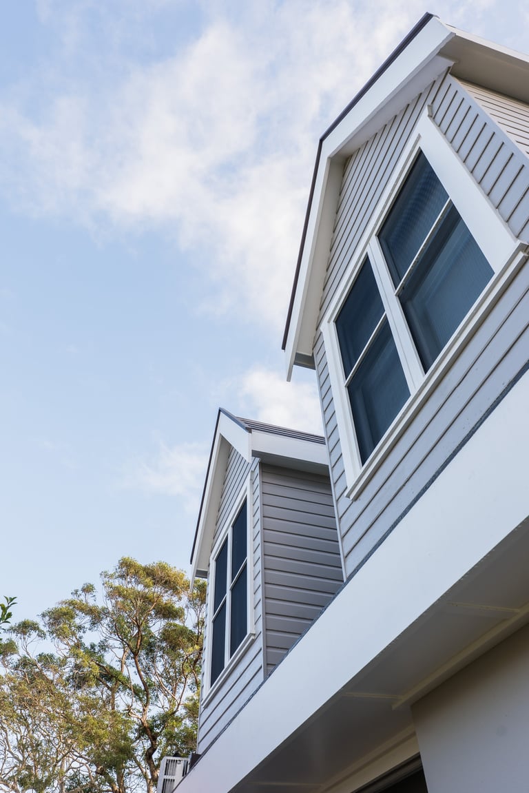 Modern white house exterior with vertical siding and stacked rectangular windows against a blue sky