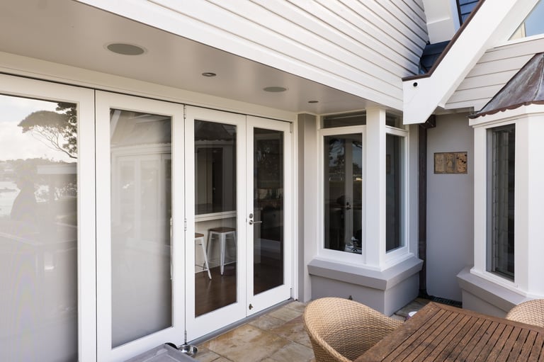 Modern sunroom with white-framed glass doors and windows, wooden deck flooring, and comfortable seating area with natural light