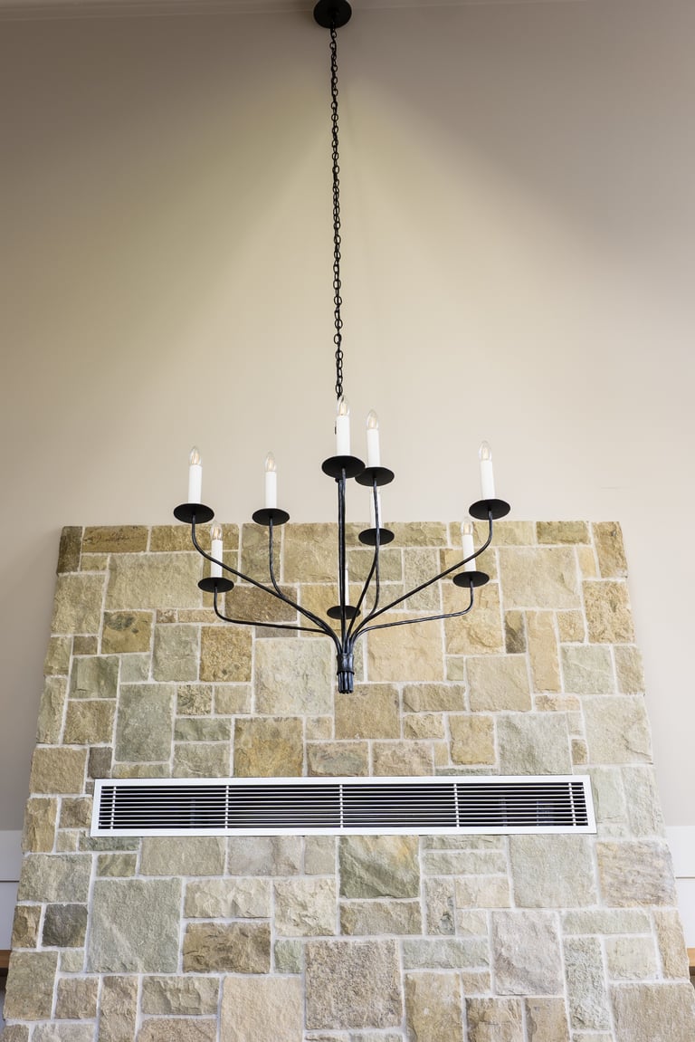 Black metal candelabra chandelier with candles hanging above a stone tile fireplace with air vent