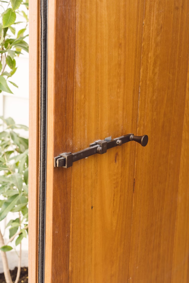 Black metal curtain rod with finial mounted on wooden wall next to green foliage