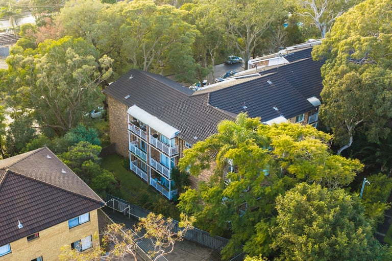 Aerial view of a modern residential building with dark roof surrounded by mature trees in a suburban neighborhood