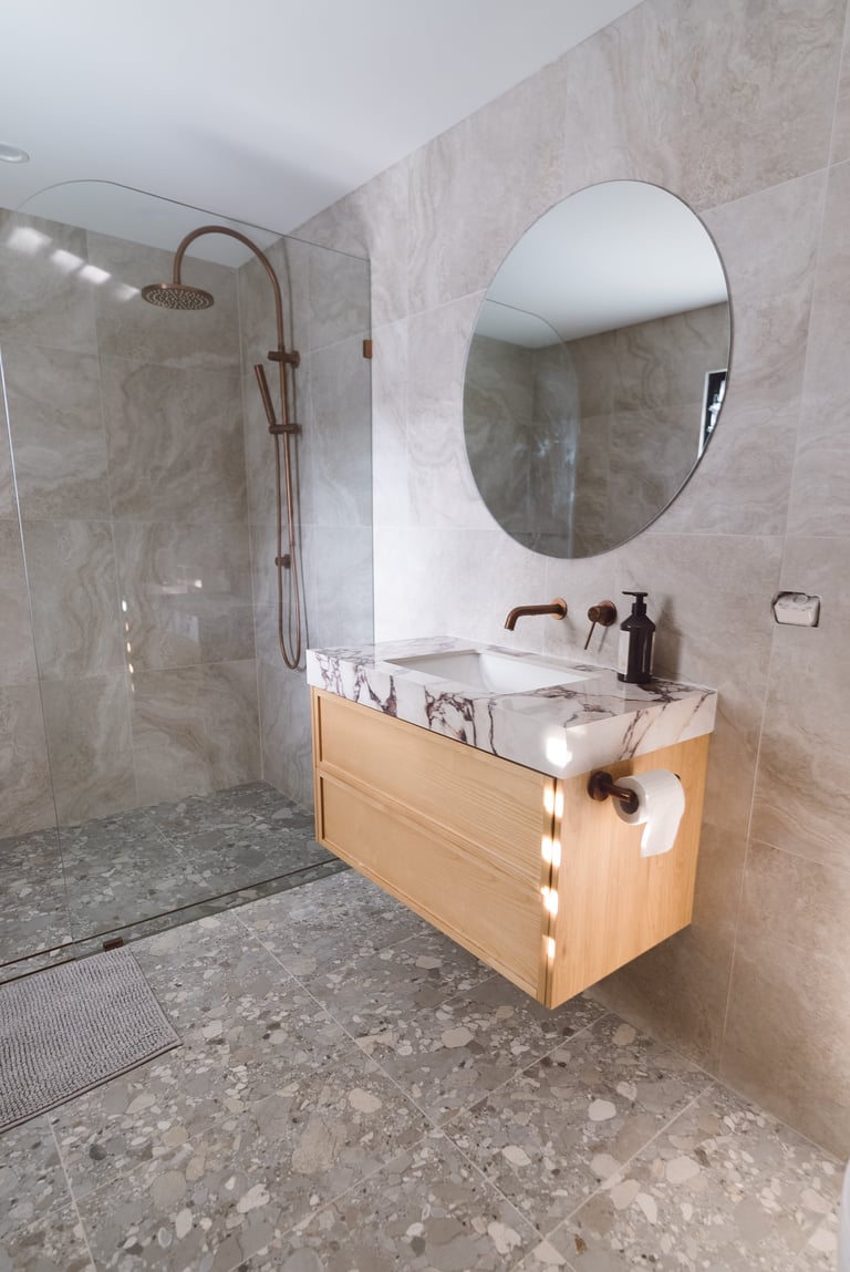 Modern bathroom with wooden vanity, oval mirror, and walk-in shower with glass enclosure and tile walls