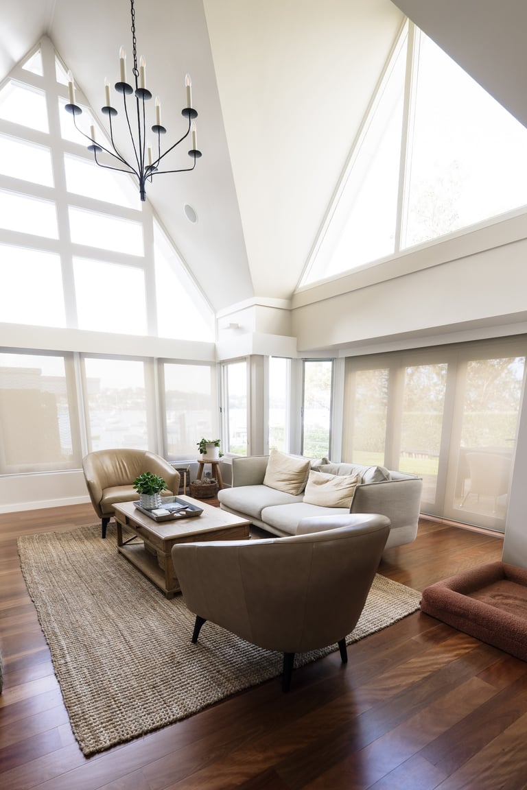 Bright modern sunroom with vaulted ceiling, skylights, contemporary chandelier, and comfortable seating arrangement with gray upholstered chairs and sofa.