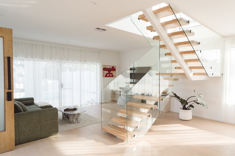 Modern open-concept living room with floating wooden staircase and glass railing, bright natural lighting from skylights and windows